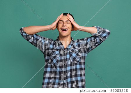 Half-length portrait of young shocked man, student standing with raising hands isolated on green studio background. Half-length portrait of young shocked man, student standing with raising hands isolated on green studio background. 85085238