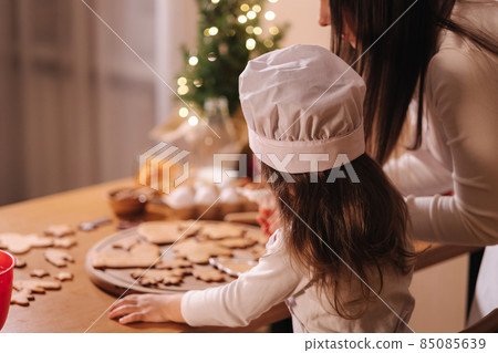 Mom with adorable little daughter spend time at kitchen in Christmas eve. Girls preparing sweets for holidays. Gingerbread and candy. Happy family Mom with adorable little daughter spend time at kitchen in Christmas eve. Girls preparing sweets for holidays. Gingerbread and candy. Happy family 85085639