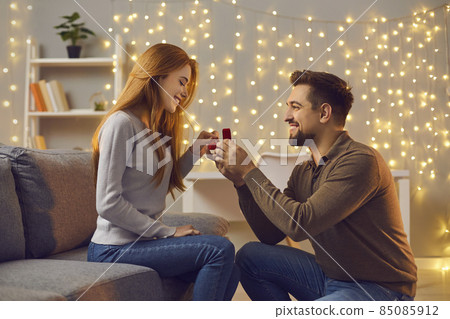 Will you marry me. Couple making love promise to each other on cozy evening at home. Happy woman getting romantic marriage proposal. Young man proposing to girlfriend and giving her engagement ring 85085912