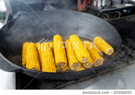 Close-up heap pile of many sweet tasty ripe boiled corn cobs cooked in cast iron cauldron on open fire coal at agricultural food fest fair on winter day outdoors. Takeaway healthy snack food Close-up heap pile of many sweet tasty ripe boiled corn cobs cooked in cast iron cauldron on open fire coal at agricultural food fest fair on winter day outdoors. Takeaway healthy snack food 85086095
