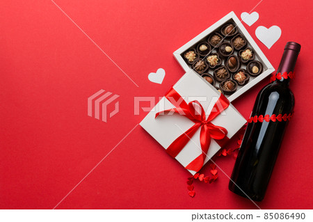Bottle of red wine on colored background for Valentine Day with gift and chocolate. Heart shaped with gift box of chocolates top view with copy space 85086490