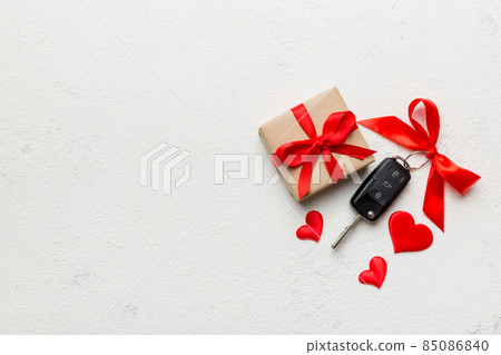 Black car key in a present box with a ribbon and red heart on colored background. Valentine day composition Top view 85086840