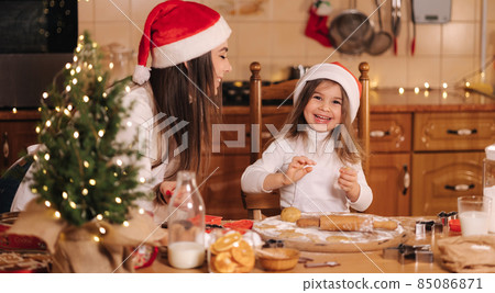 Process of mom and daughter baking at home. Raw dough for cooking Christmas cookies gingerbread on wooden table. Candle light at evening time. Fir tree 85086871