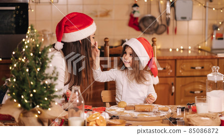 Process of mom and daughter baking at home. Raw dough for cooking Christmas cookies gingerbread on wooden table. Candle light at evening time. Fir tree 85086872