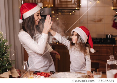 Two girls in santa hat spent time very happy at the kitchen. Christmas holidays Two girls in santa hat spent time very happy at the kitchen. Christmas holidays 85086885