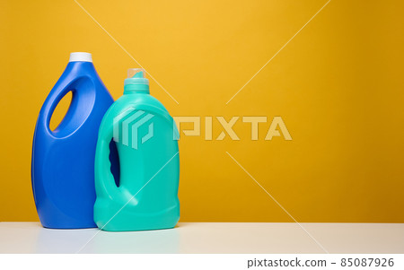 plasticd blue large bottles with liquid detergent stand on a white table, yellow background plasticd blue large bottles with liquid detergent stand on a white table, yellow background 85087926