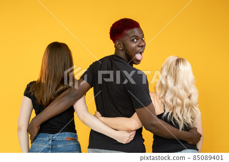 Open relationship. Casanova man. Multiracial love. Date luck. Lovelace successful amazed happy guy embracing two different women together isolated on orange background. Open relationship. Casanova man. Multiracial love. Date luck. Lovelace successful amazed happy guy embracing two different women together isolated on orange background. 85089401