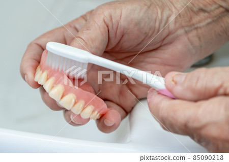 Asian senior or elderly old woman patient use toothbrush to clean partial denture of replacement teeth. Asian senior or elderly old woman patient use toothbrush to clean partial denture of replacement teeth. 85090218