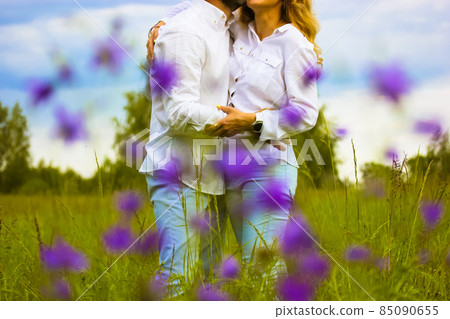 Beautiful couple in love gently embracing standing in a green blossoming meadow in summer. Husband, wife in white shirts showing their feelings for each other. Devotion, purity, harmony, love concept. Beautiful couple in love gently embracing standing in a green blossoming meadow in summer. Husband, wife in white shirts showing their feelings for each other. Devotion, purity, harmony, love concept. 85090655