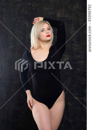 Young blonde plump woman with bright makeup in black bodysuit at dark background 85090792