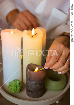Woman lighting fire on white and green soy, wax scented candles, holding burning match in hand. Cozy home. Romantic mood, preparing for date. Christmas evening, New Year 2022 vertical photo. Spa time. Woman lighting fire on white and green soy, wax scented candles, holding burning match in hand. Cozy home. Romantic mood, preparing for date. Christmas evening, New Year 2022 vertical photo. Spa time. 85091062