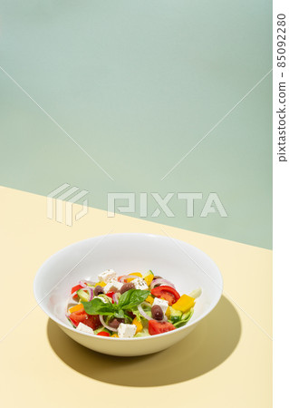 Greek salad in white plate hard shadows on blue and yellow 85092280