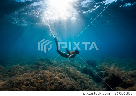 Freediver woman with fins glides underwater in tropical blue. 85095393