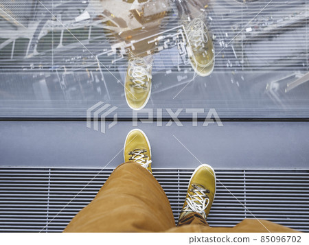 Top view on man's feet in yellow leather sneakers. Man stands near panoramic window on high floor of building. Urban fashion of millennials. 85096702