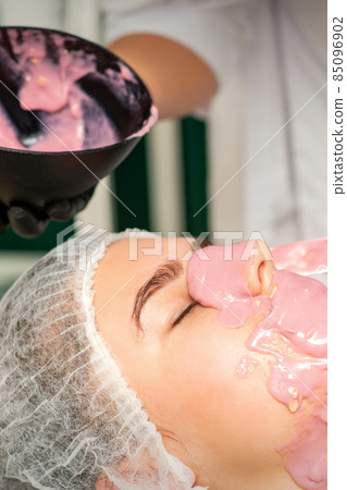 The cosmetologist applying an alginate mask to the face of a young woman in a beauty salon. The cosmetologist applying an alginate mask to the face of a young woman in a beauty salon. 85096902