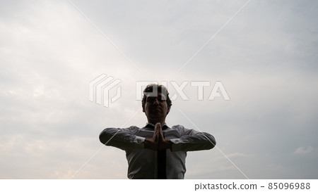 Young businessman meditating under grey sky 85096988