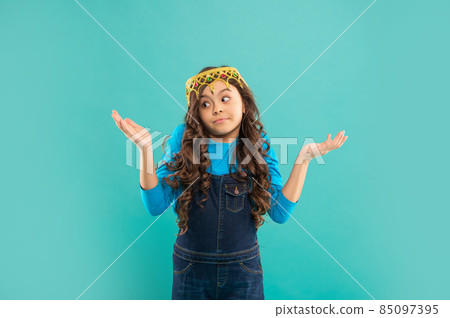 kid with curly hair in princess crown making choice on blue background with copy space, choose 85097395