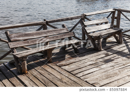 Old wooden benches stand at the end of a pier 85097884
