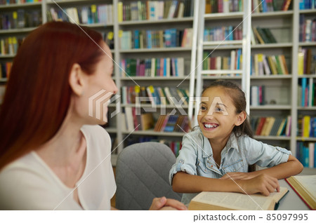 Smiling girl looking at woman sitting at table 85097995