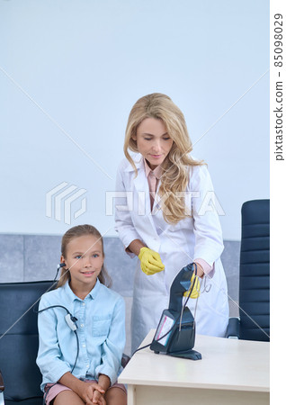 Woman doctor standing near sitting girl in earpiece Woman doctor standing near sitting girl in earpiece 85098029