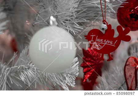 Beautiful Christmas red and silver balls on a white Christmas tree with decorations in the form of ribbons with the inscriptions Merry Christmas and Happy New Year 85098097