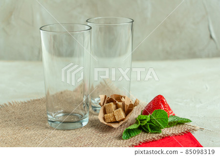 empty cocktail glasses on burlap napkin, strawberries, mint and brown sugar empty cocktail glasses on burlap napkin, strawberries, mint and brown sugar 85098319