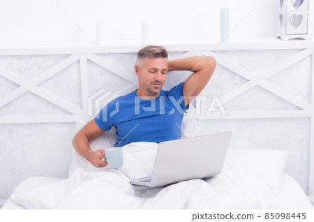 Relaxation in bed. Happy man drink coffee using laptop. Morning relaxation Relaxation in bed. Happy man drink coffee using laptop. Morning relaxation 85098445