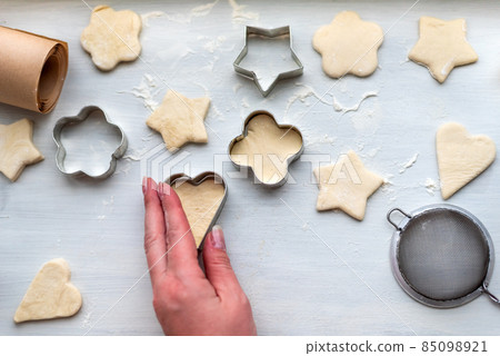 Top view of woman hands cooking a gingerbread cookie in the form of heart, star, cloud and flower. Christmas and New Year concept, festive preparations for winter hilodays 85098921