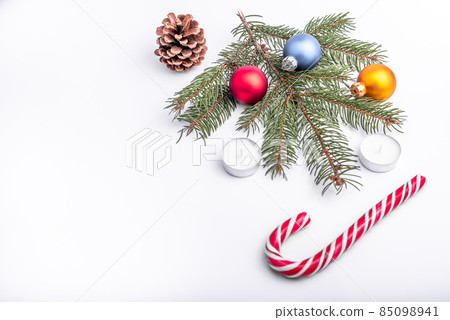 Christmas and new year flat lay: green fir branch, cone, red, blue and yellow balls, two candles and caramel candy on white isolated background. Christmas and new year flat lay: green fir branch, cone, red, blue and yellow balls, two candles and caramel candy on white isolated background. 85098941