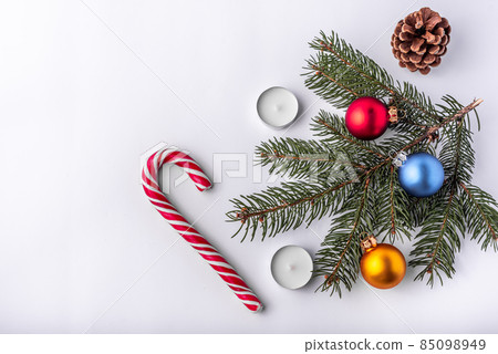 Christmas and new year flat lay: green fir branch, cone, red, blue and yellow balls, two candles and caramel candy on white isolated background. Christmas and new year flat lay: green fir branch, cone, red, blue and yellow balls, two candles and caramel candy on white isolated background. 85098949