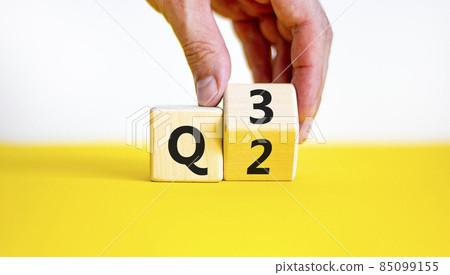 From 2nd to 3rd quarter symbol. Businessman turns a wooden cube and changes words 'Q2' to 'Q3'. Beautiful yellow table, white background. Business, happy 3rd quarter Q3 concept, copy space. From 2nd to 3rd quarter symbol. Businessman turns a wooden cube and changes words 'Q2' to 'Q3'. Beautiful yellow table, white background. Business, happy 3rd quarter Q3 concept, copy space. 85099155