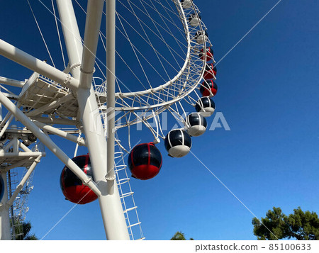 Closeup modern Ferris wheel against blue sky and white clouds. Ferris wheel at funfair for entertainment and recreation on holiday. Modern construction of Ferris wheel in amusement. Fun festival Closeup modern Ferris wheel against blue sky and white clouds. Ferris wheel at funfair for entertainment and recreation on holiday. Modern construction of Ferris wheel in amusement. Fun festival 85100633