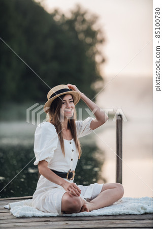 Portrait of a happy caucasian woman in a white dress and hat outdoors sitting and smiling. Portrait of a happy caucasian woman in a white dress and hat outdoors sitting and smiling. 85100780