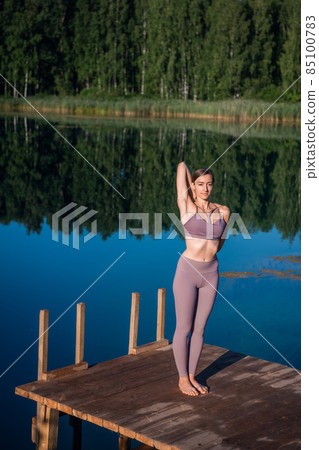 Young Woman practicing yoga on the wooden berth at lake. Single sport healthy training on nature at sunny weather 85100783