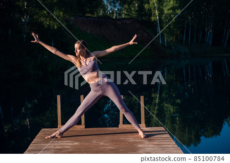 Woman doing yoga on a forest lake. Beautiful girl doing exercises on stretching and flexibility outdoors Woman doing yoga on a forest lake. Beautiful girl doing exercises on stretching and flexibility outdoors 85100784