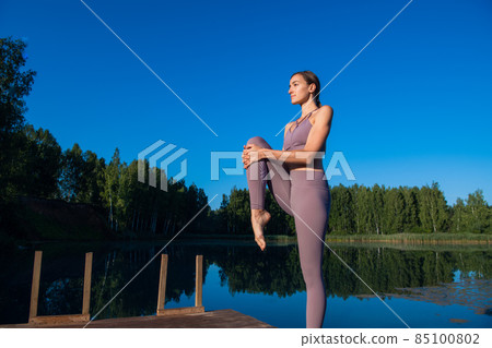 Beautiful young woman performing a spiritual yoga pose on a forest lake at sunny day, sunrise zen wellness Beautiful young woman performing a spiritual yoga pose on a forest lake at sunny day, sunrise zen wellness 85100802