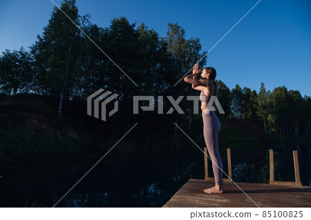 Beautiful young woman performing a spiritual yoga pose on a forest lake at sunny day, sunrise zen wellness Beautiful young woman performing a spiritual yoga pose on a forest lake at sunny day, sunrise zen wellness 85100825