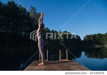 Young female practicing yoga against the sky on a sunrise. Pretty slim woman performs an exercise. Healthcare, meditaion, welness, mindfulness concept. Young female practicing yoga against the sky on a sunrise. Pretty slim woman performs an exercise. Healthcare, meditaion, welness, mindfulness concept. 85100826