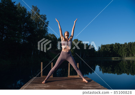Young Woman practicing yoga on the wooden berth at lake. Single sport healthy training on nature at sunny weather Young Woman practicing yoga on the wooden berth at lake. Single sport healthy training on nature at sunny weather 85100828