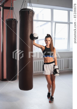 Female kickboxer hitting punching bag while dust particles flies in sunflare light background. Female kickboxer hitting punching bag while dust particles flies in sunflare light background. 85100878