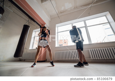 Female martial arts fighter practicing with trainer, punching taekwondo kick pad exercise kicking. Training of kickboxer woman strikes with bare foot mitts punching bag kicking shield Female martial arts fighter practicing with trainer, punching taekwondo kick pad exercise kicking. Training of kickboxer woman strikes with bare foot mitts punching bag kicking shield 85100879