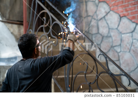 Man in safety glasses is welding metal of staircase. Welding work on metal in private house. blurred background. 85103031