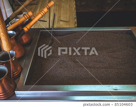 Sand for making an oriental coffee with a metal spoon in it and many Turks standing on the side 85104603