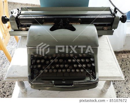Antique gray typewriter with Cyrillic letters and one missing key stands on a white wooden table 85107672