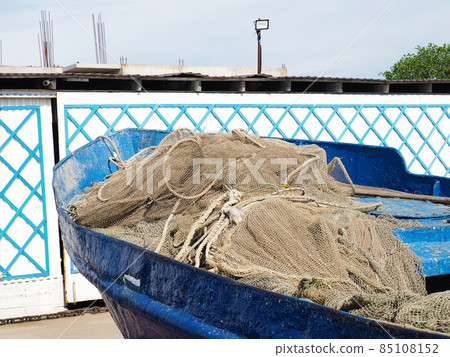 A rolledup fishing net lies in an old blue shabby boat in the bright sun outdoors A rolledup fishing net lies in an old blue shabby boat in the bright sun outdoors 85108152