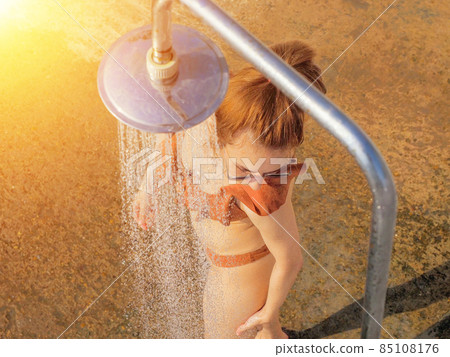 A woman in a bikini is washing herself under a shower outdoors on a sunny day. Beach shower 85108176