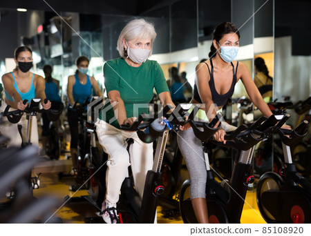 Women wearing masks training on stationary bikes Women wearing masks training on stationary bikes 85108920