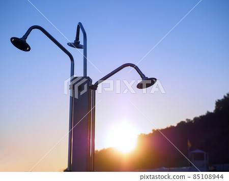 Triple beach shower against the backdrop of the sun setting behind the mountains and clear sky 85108944