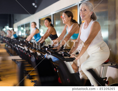 Mature woman taking cycling class at gym Mature woman taking cycling class at gym 85109265