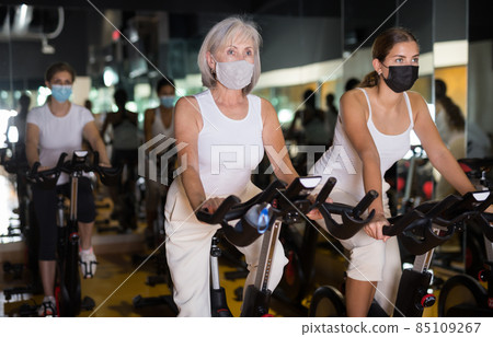 Girl and her mother in masks on fitness bikes in gym 85109267